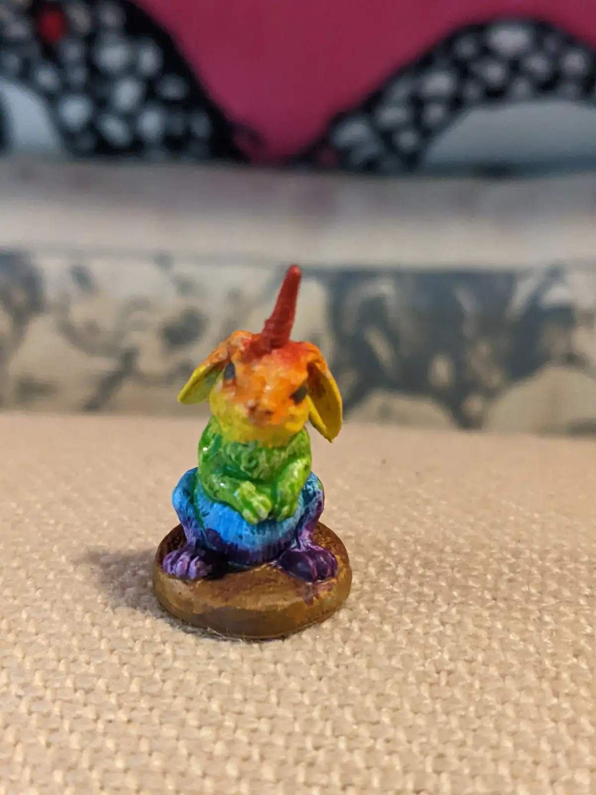 A small, hand-painted figurine of a rabbit with a rainbow gradient color scheme and a red horn on its head, sitting on a…