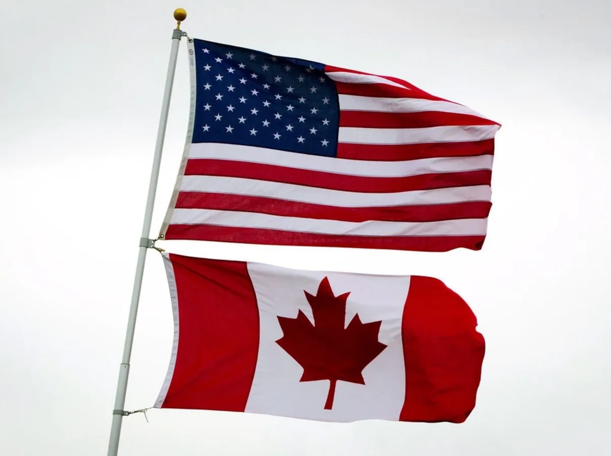 Two national flags, the United States flag with its stars and stripes and the Canadian flag with its red maple leaf, are…