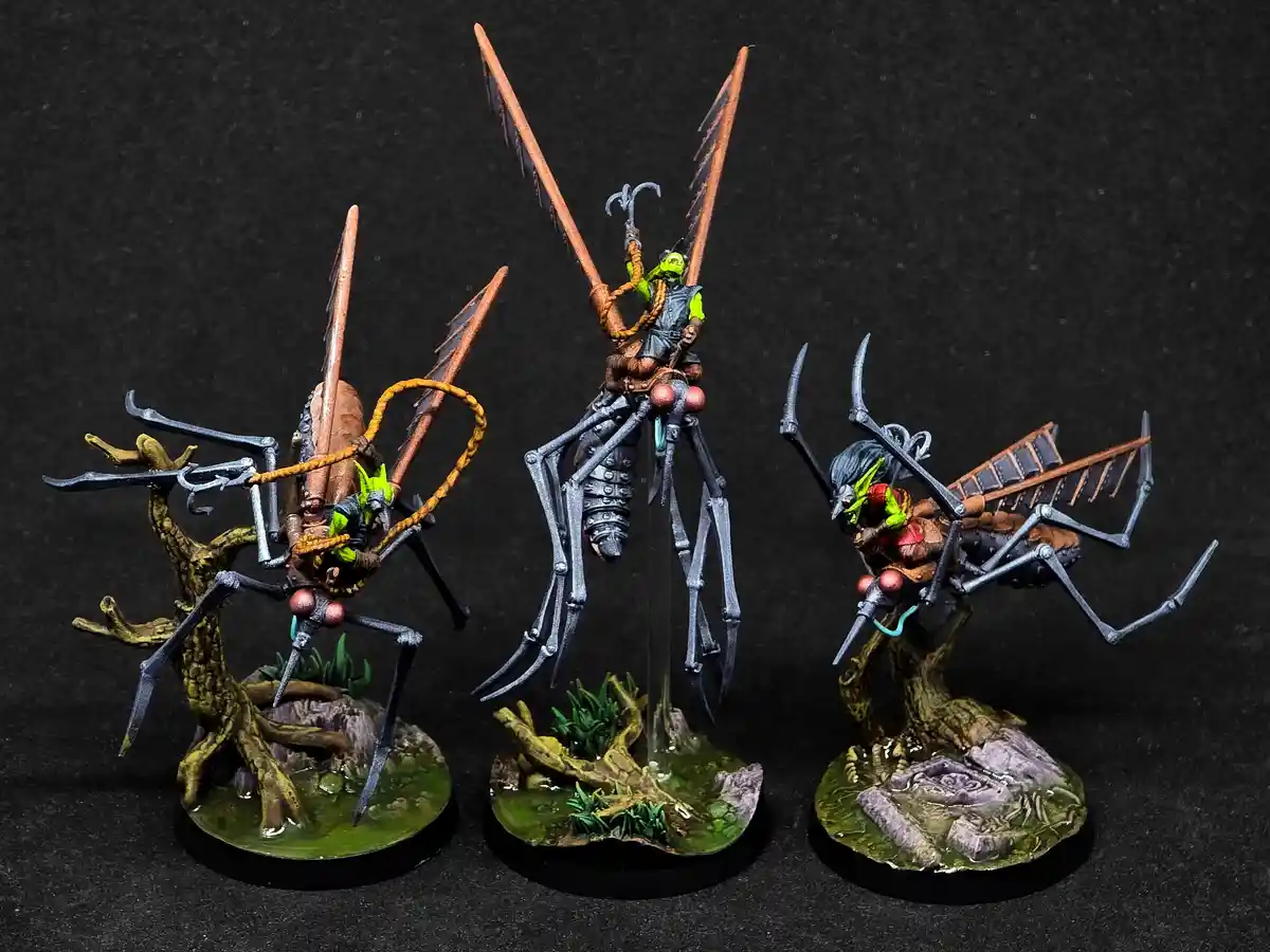 Three intricately painted miniature figures show green-skinned fantasy orcs riding large, biomechanical insectoid mounts…