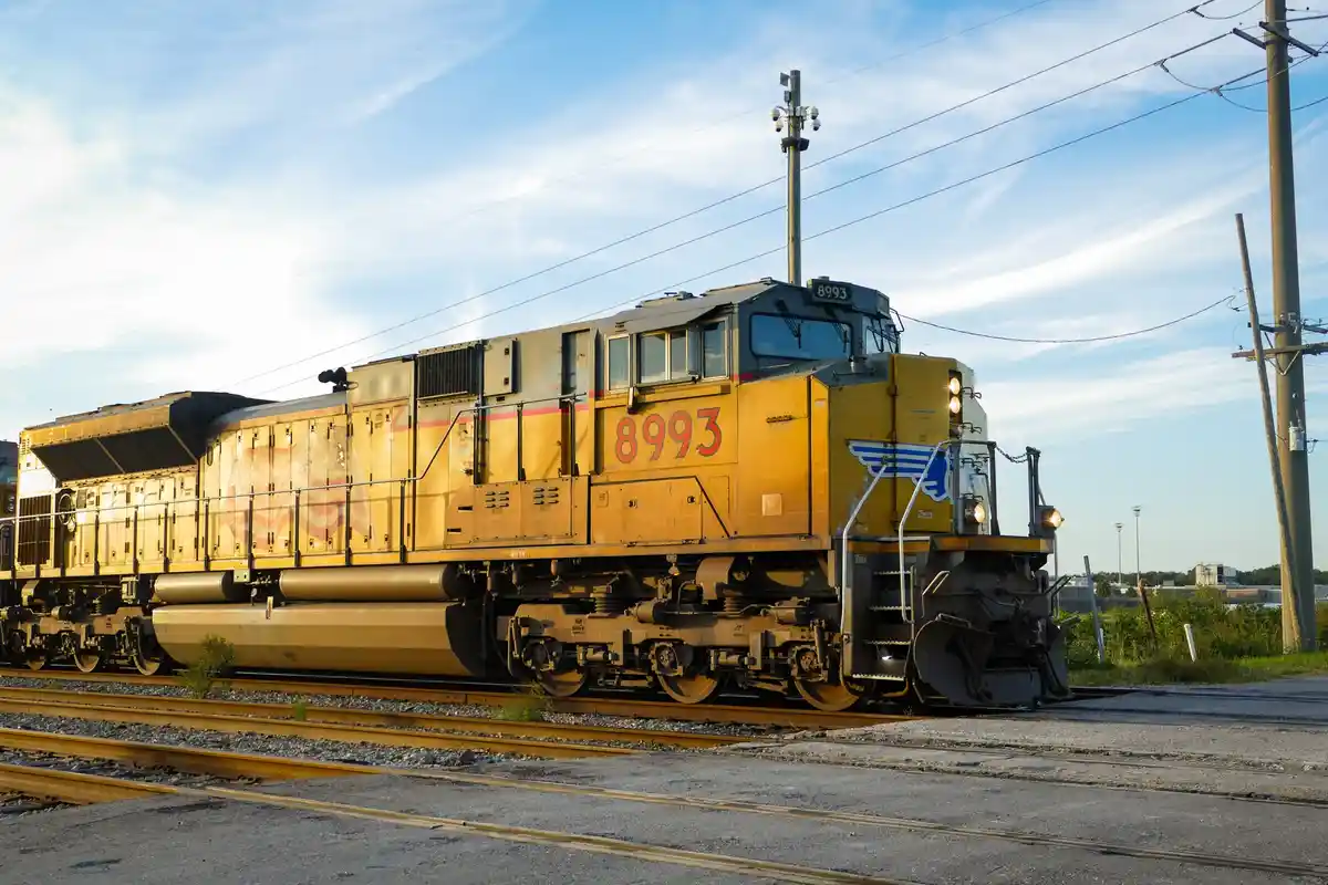 A yellow freight train engine, numbered 8993, sits on tracks under a partly cloudy sky, with utility poles and wires in the…