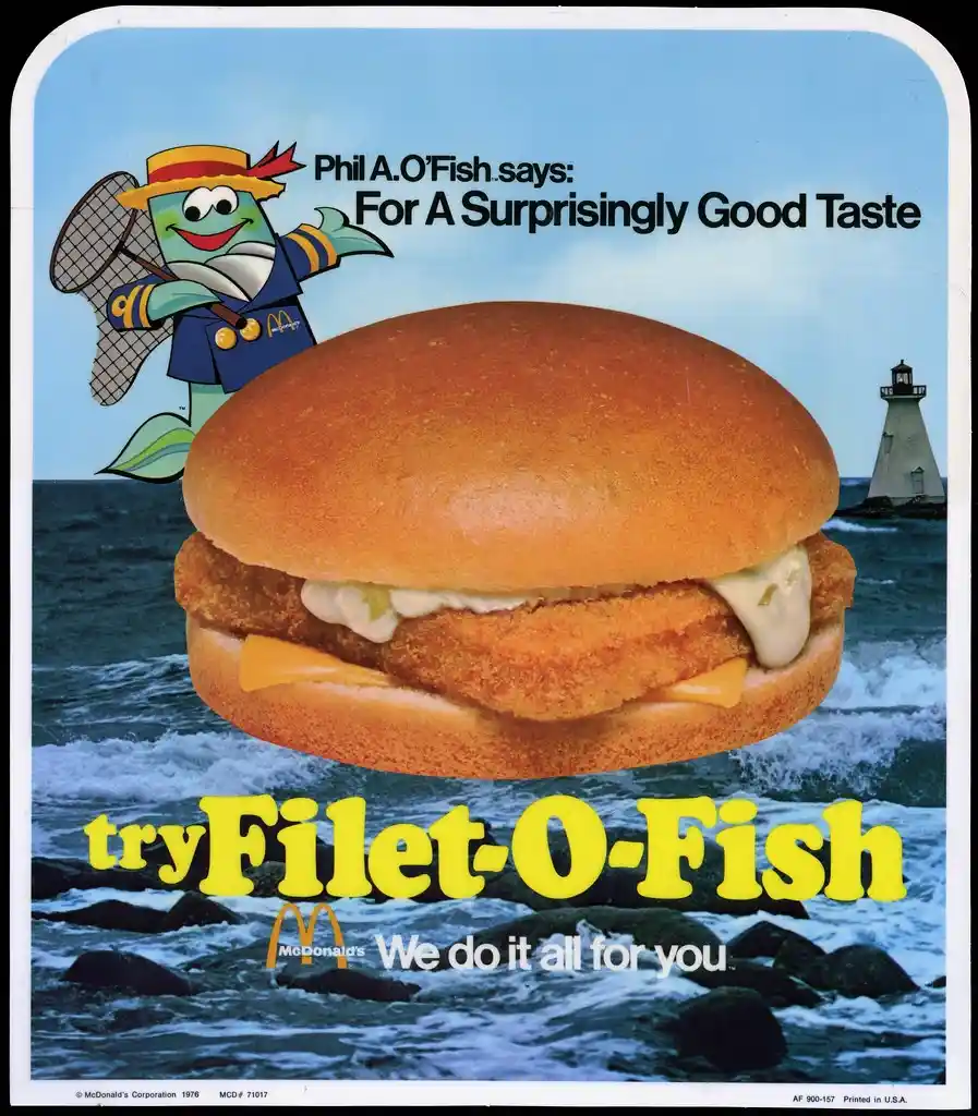 A vintage 1976 McDonald's advertisement featuring a large Filet-O-Fish burger floating over ocean waves with a lighthouse in…
