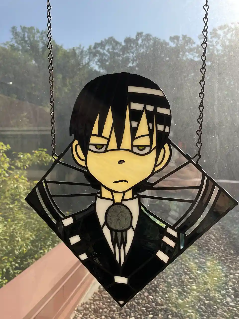 A stained glass window hanging from chains shows a stylized anime character with black hair, yellow skin, and a stern…
