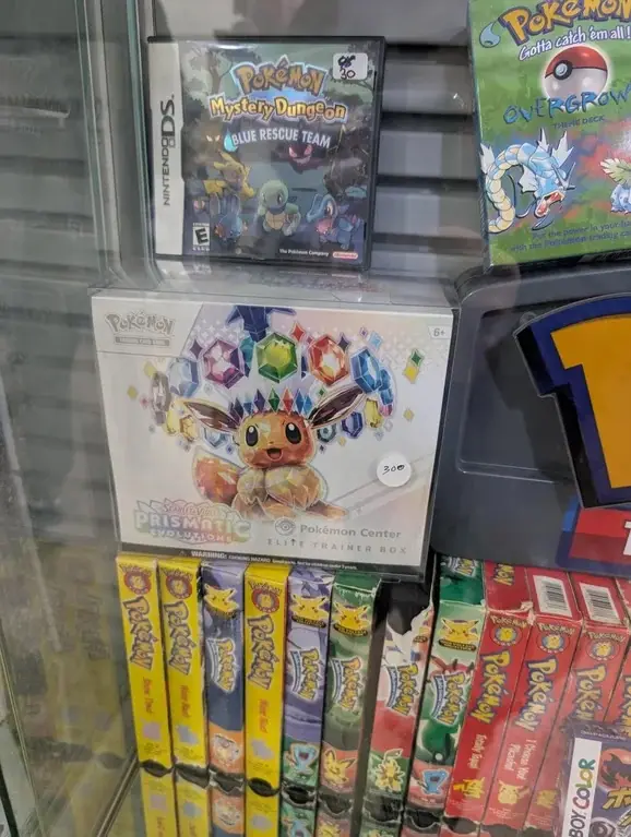 A shelf in a Pokémon store displays a Nintendo DS game case for 'Pokémon Mystery Dungeon: Blue Rescue Team' priced at $30…