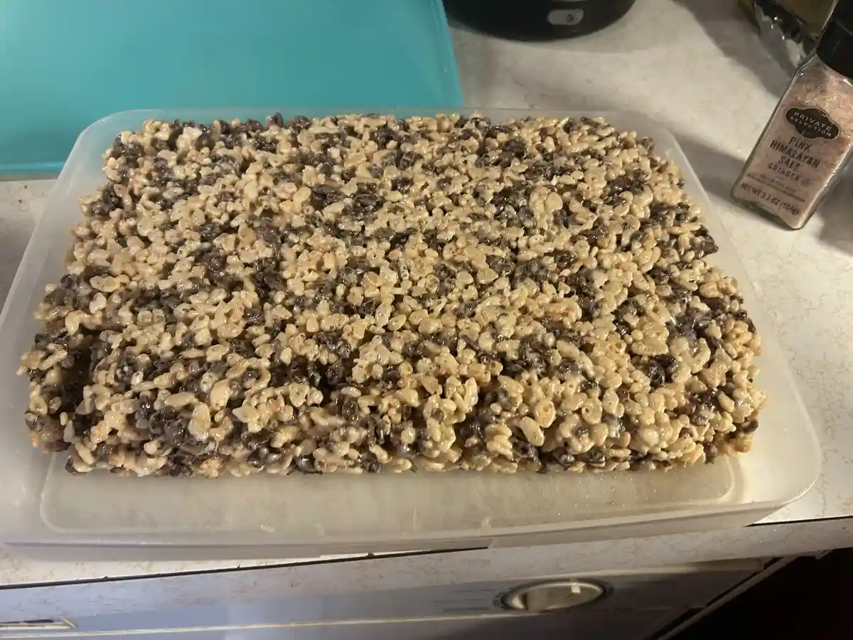 A rectangular pan of homemade rice krispies treats sits on a kitchen counter, featuring a distinct pattern of alternating…