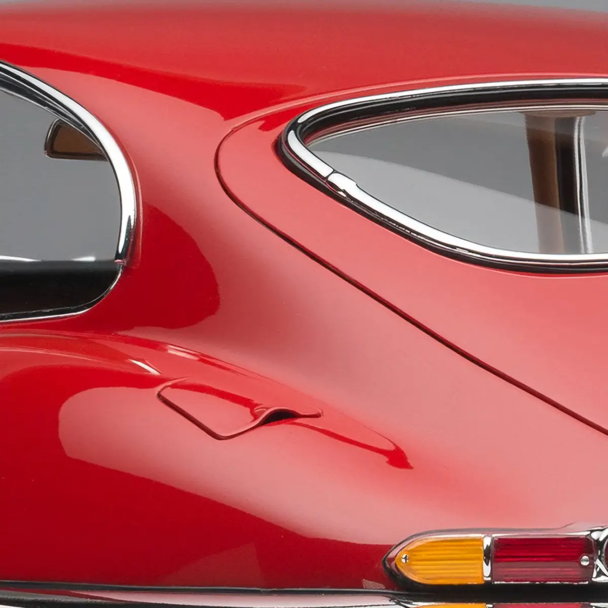 A close-up of a glossy red classic car's rear quarter panel, showing chrome-trimmed windows, a sleek body line, and a…