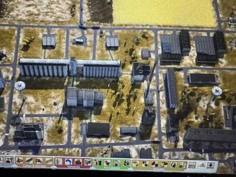An overhead view of a city in a simulation game, showing a grid of roads and buildings, with a single road running through…
