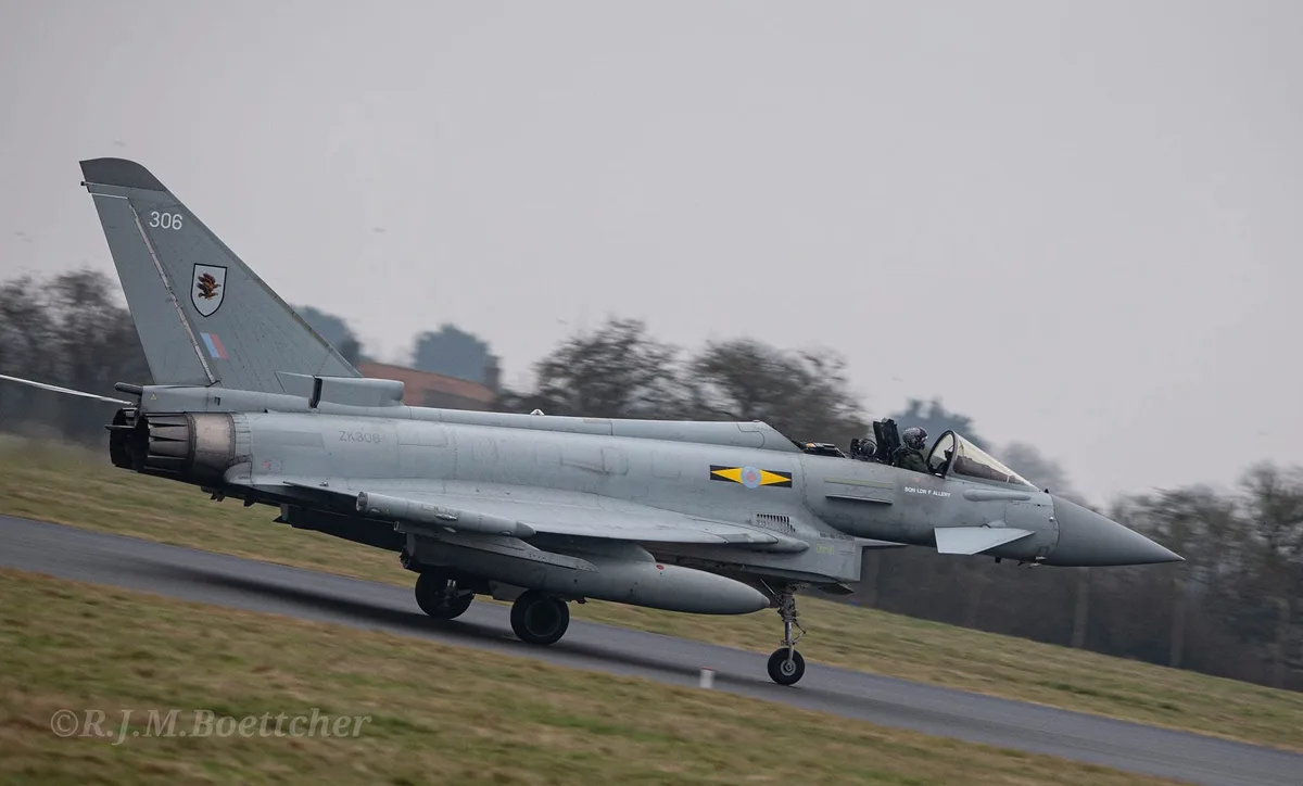A grey Eurofighter Typhoon jet fighter is shown taxiing on a runway, with a pilot visible in the cockpit. The aircraft has…