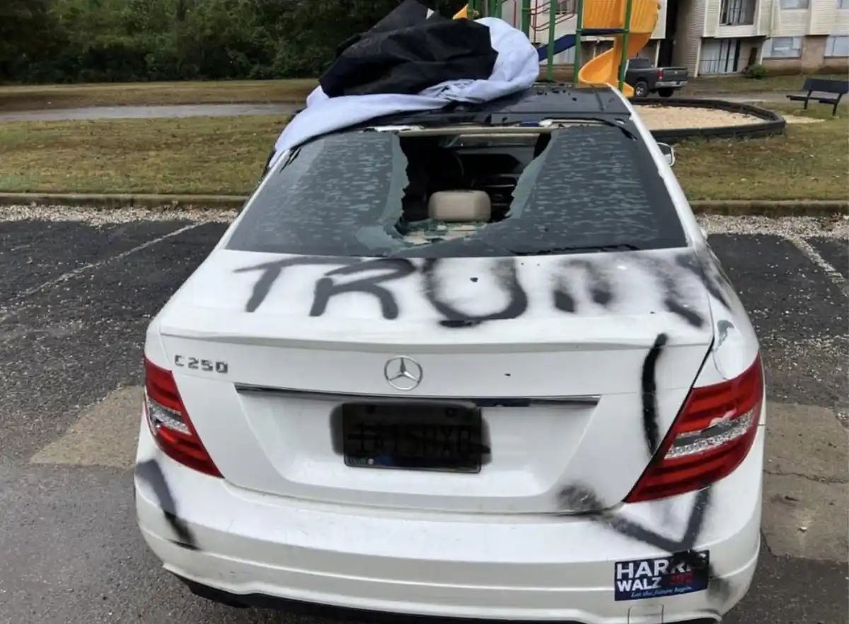 The rear of a white Mercedes-Benz C250 is shown with its rear window shattered and covered in black spray-painted graffiti…