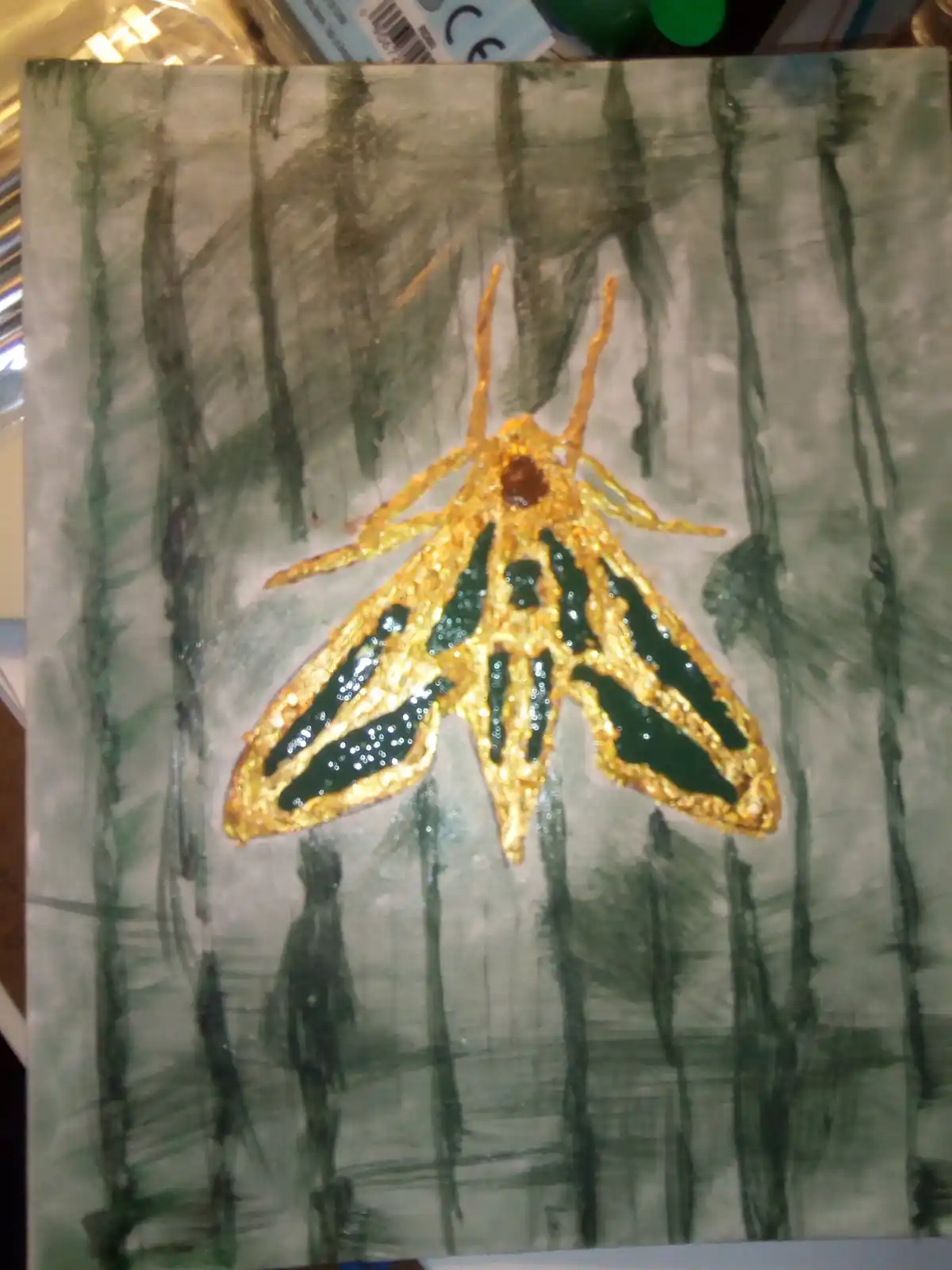 A hand-painted artwork depicts a moth with glittery gold wings and black patterns, set against a sketchy background of tree…