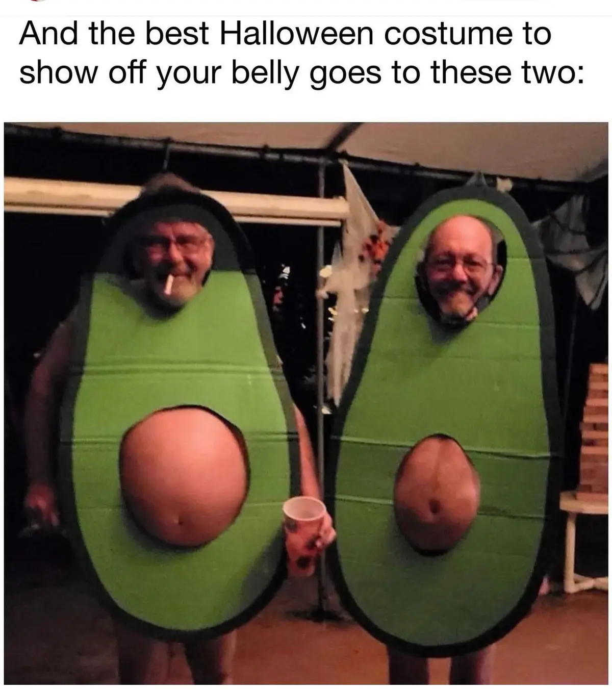 Two men in avocado costumes stand side-by-side, their bellies prominently displayed through cutouts in the green…