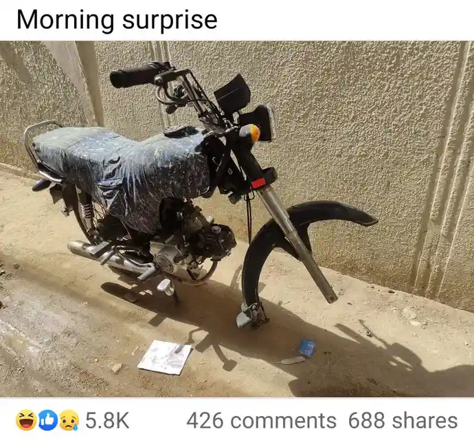 A motorcycle is parked outdoors against a textured wall, its seat covered with a blue patterned cloth, and its front fender…
