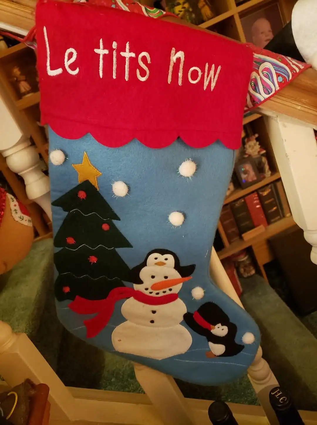 A festive blue Christmas stocking with a red top, hanging on a wooden chair, features embroidered winter scenes including a…