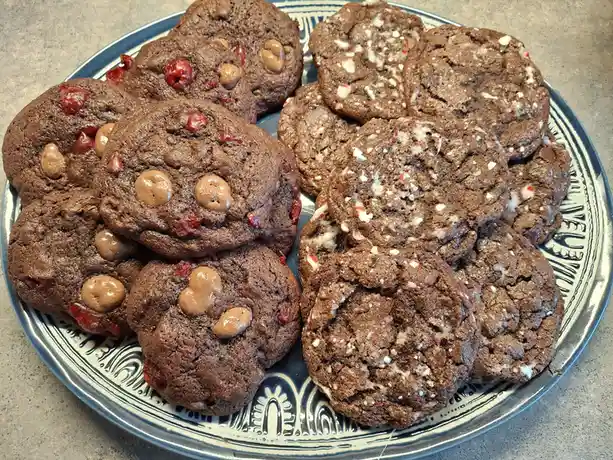 A plate of chocolate cookies is split into two distinct groups: on the left, cookies with peanut butter cups and dried…