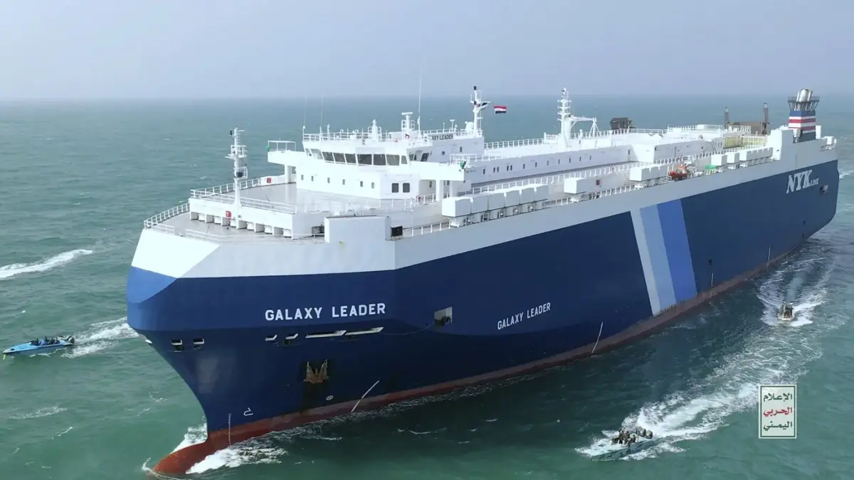 A large blue and white cargo ship named 'GALAXY LEADER' sails on the ocean, with 'NYK LINE' visible on its side. Several…