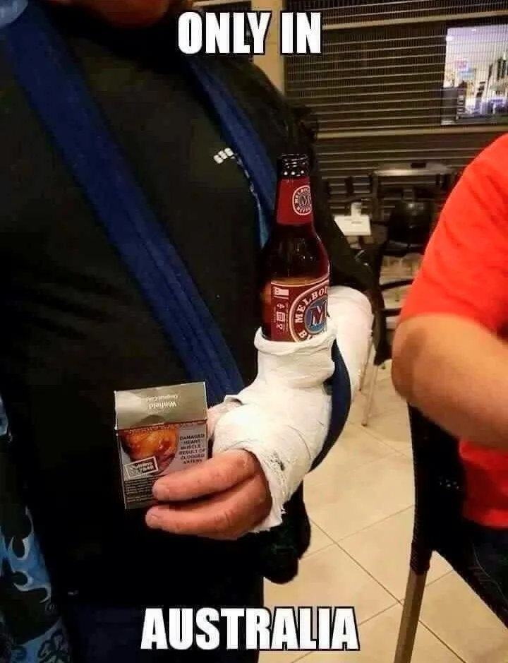 A person with a heavily bandaged right hand holds a bottle of beer in the cast and a pack of cigarettes in their left hand…