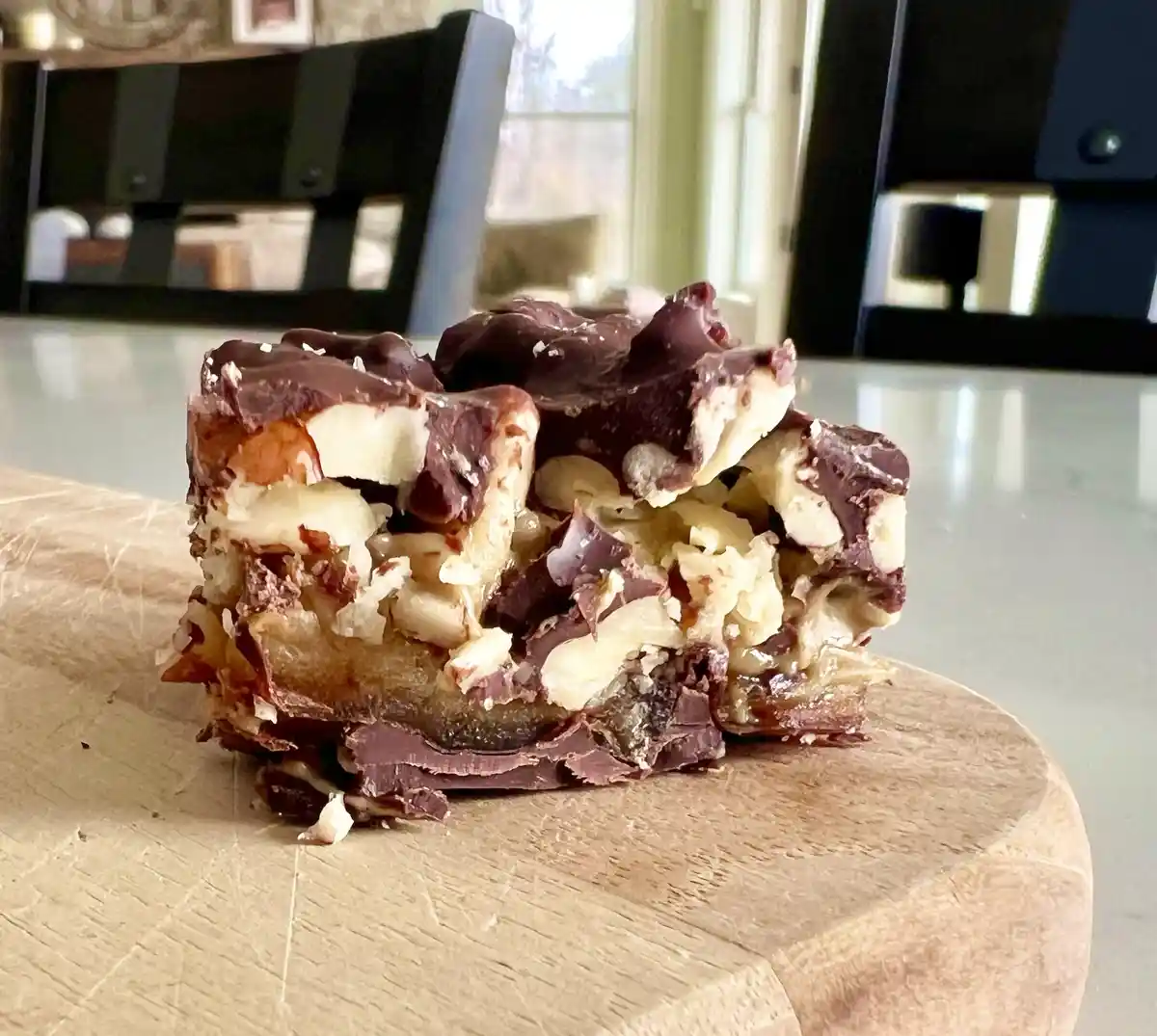 A close-up photo shows a chunky, homemade-looking bar with visible layers of chocolate, peanut butter, and chopped nuts…