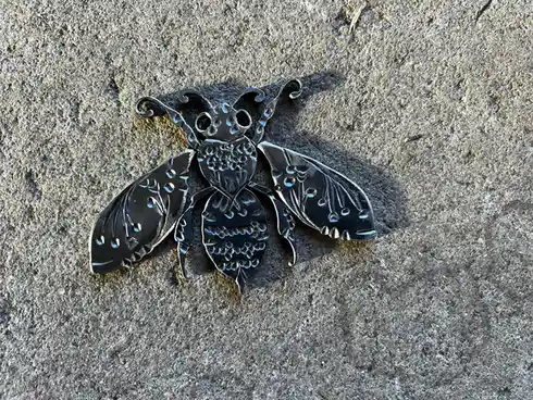 A decorative, ornate metal bee brooch or pin with detailed wings and body rests on a rough, textured concrete surface. The…