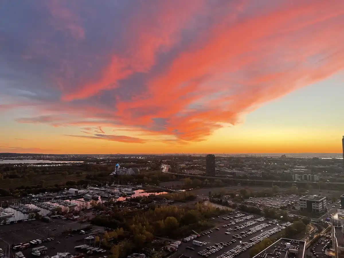 An aerial photo captures a stunning sunset over a cityscape, with vibrant orange and pink clouds dominating the sky above a…