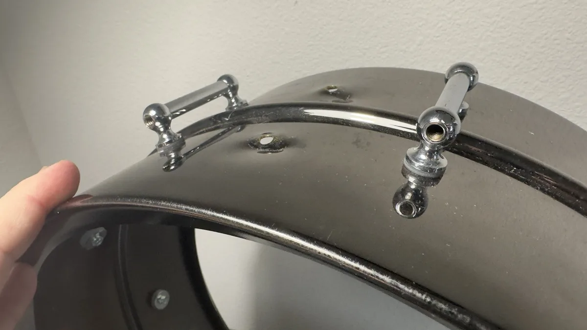 A close-up photo shows a person's thumb holding a shiny chrome motorcycle fender, which has a chrome rod attached to its top…