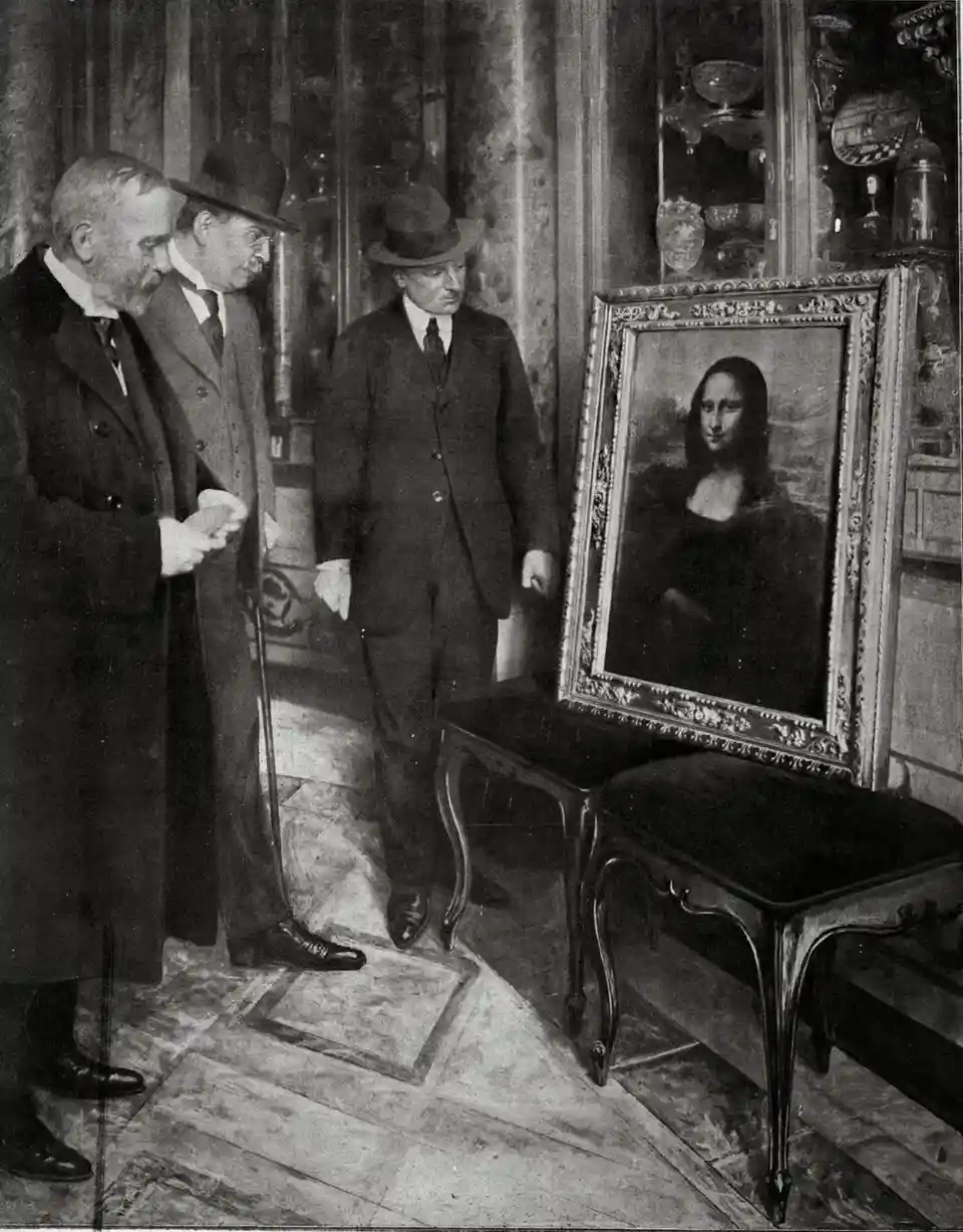 a black-and-white historical photograph shows three men in early 20th-century formal attire standing in an ornate room…