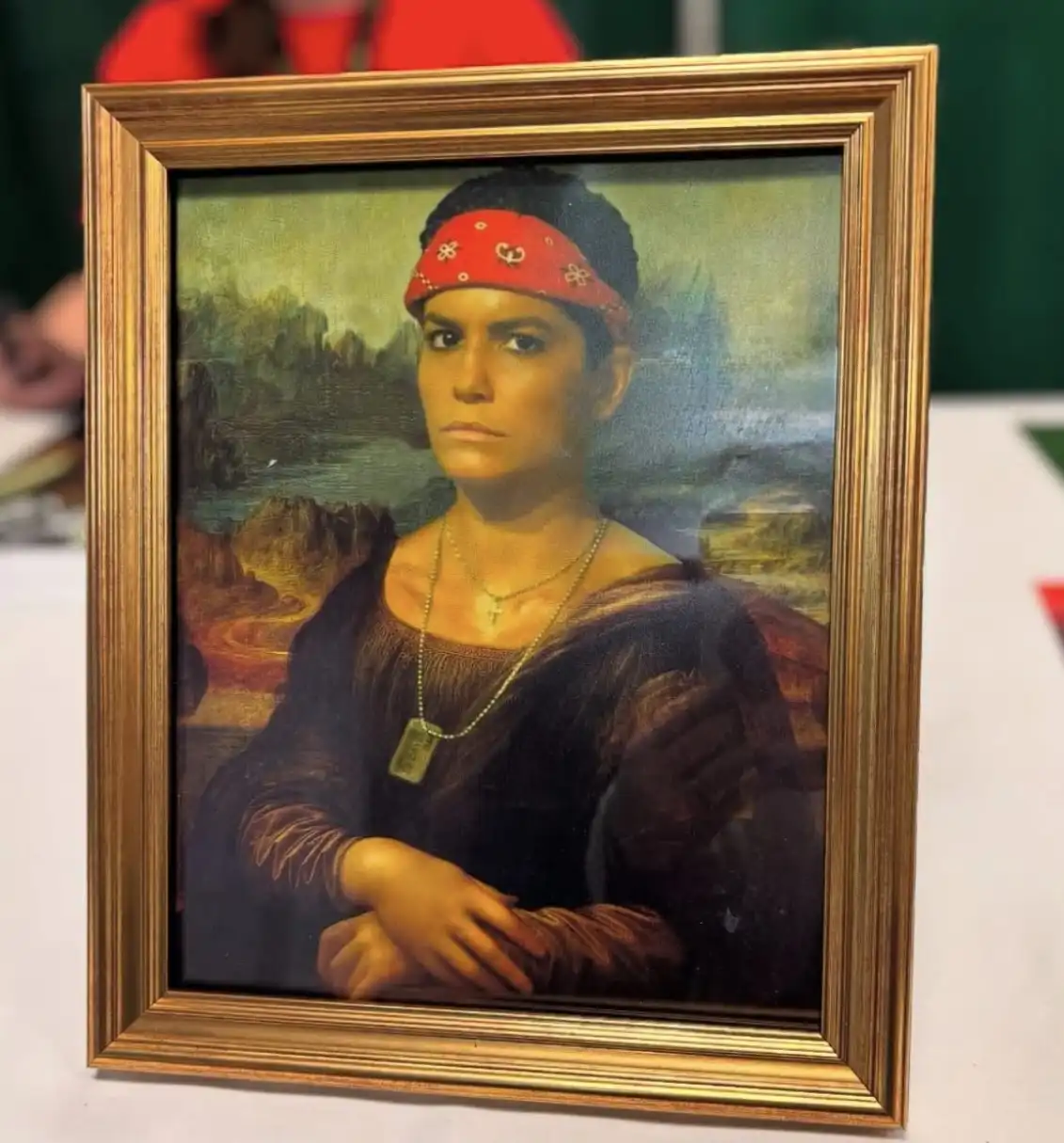 A framed painting depicts a person resembling the Mona Lisa, but with a red bandana on their head and a dog tag necklace…