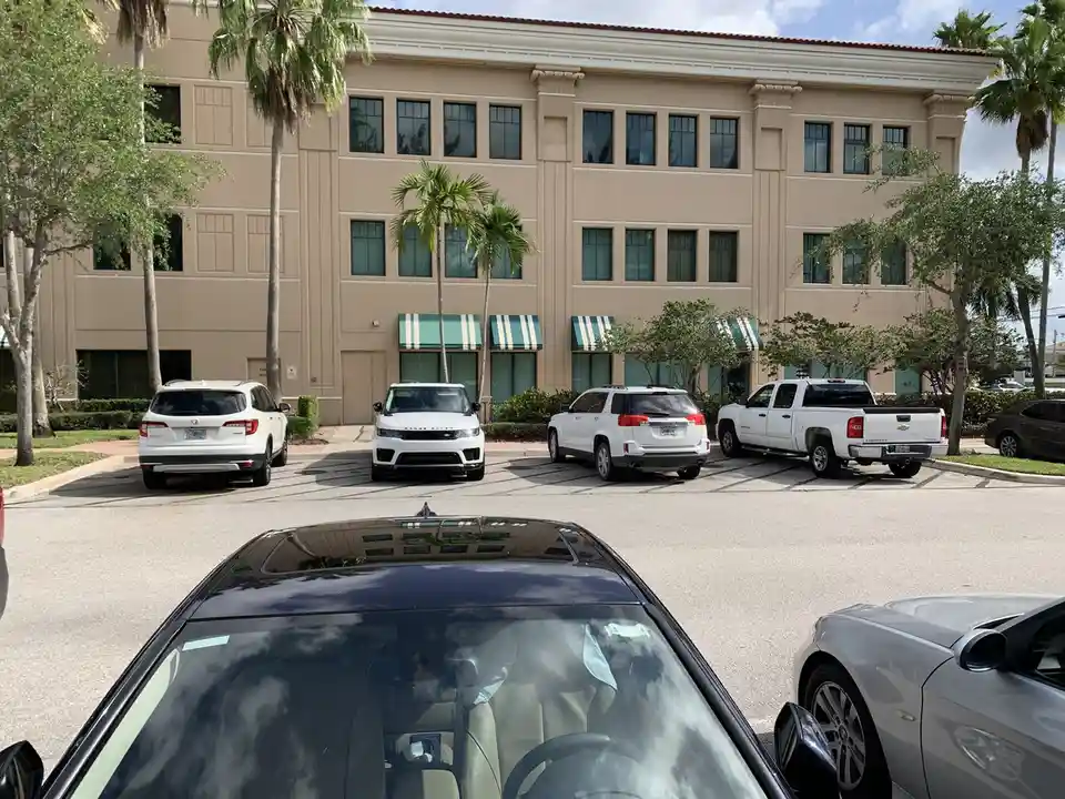 A photo taken from inside a car looking out at a parking lot with several expensive-looking white vehicles parked in front…