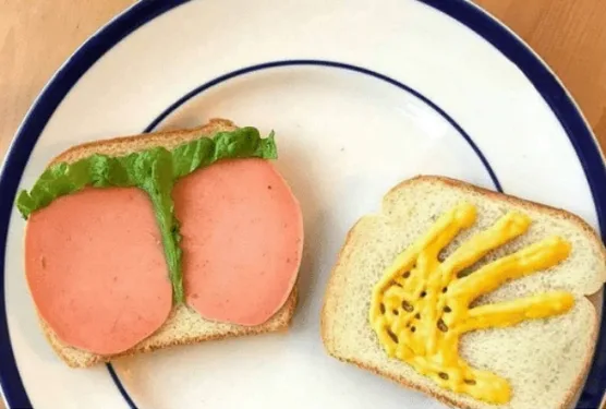 Two slices of bread on a white plate with a blue rim. One slice has two round slices of pink deli meat and a green lettuce…