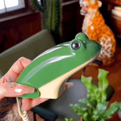a person holds a green frog-shaped telephone, showing its closed form, then opening its 'mouth' to reveal a standard numeric…
