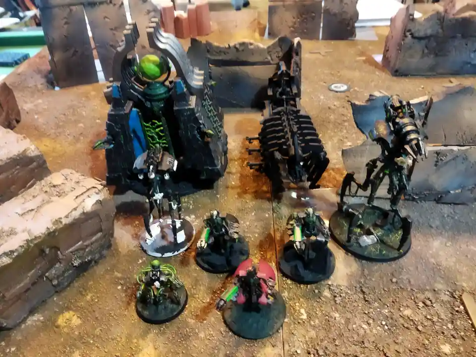 A tabletop wargaming scene featuring painted miniatures of biomechanical alien warriors and a large, ornate structure with a…