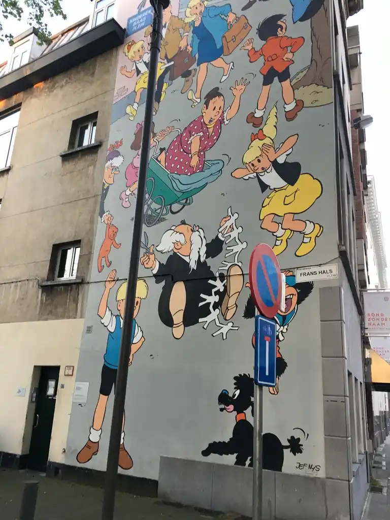 A large mural on a building wall depicts classic Belgian comic characters like Tintin, Snowy, and Captain Haddock in…
