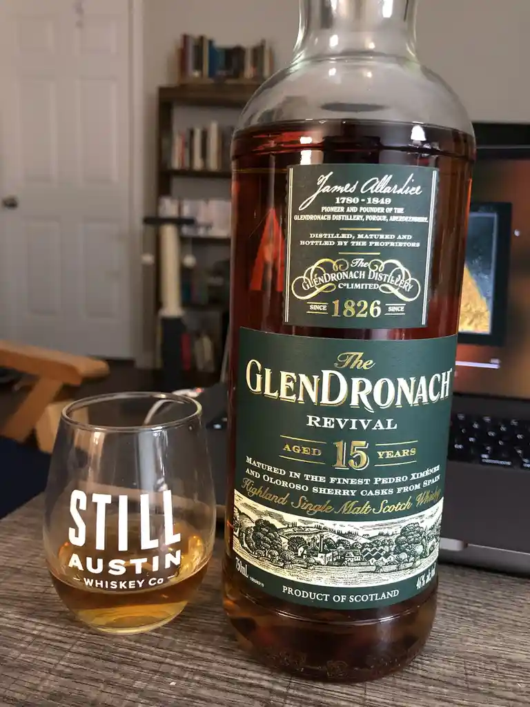A bottle of Glendronach Revival 15-year-old Highland Single Malt Scotch Whisky sits next to a glass labeled 'STILL AUSTIN…