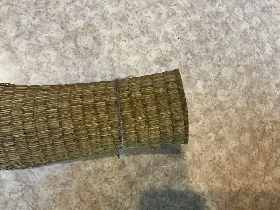 A close-up photo shows a rolled-up, woven bamboo or straw mat lying on a speckled beige countertop. A frayed, gray string is…