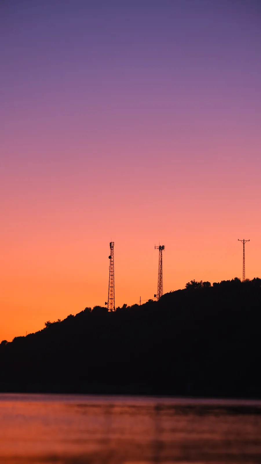 A serene sunset photo shows a gradient sky transitioning from deep purple to vibrant orange, silhouetting a hilltop with…