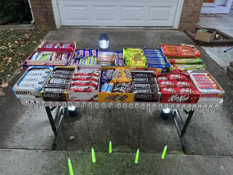 An outdoor setup features a white xylophone-like instrument with numerous candy bars arranged in boxes across its keys…