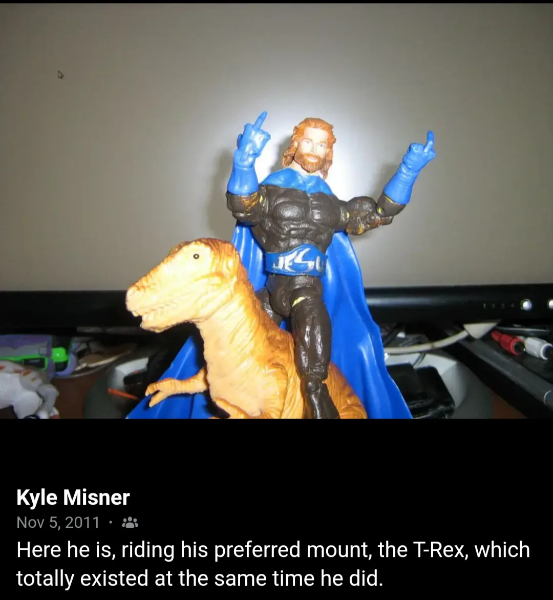 A plastic action figure of a muscular man with long hair and a beard, wearing a blue cape and a belt with 'JESU' written on…