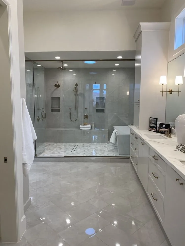 A luxurious, modern bathroom with large gray marble tiles on the floor and walls, a spacious walk-in shower with glass doors…