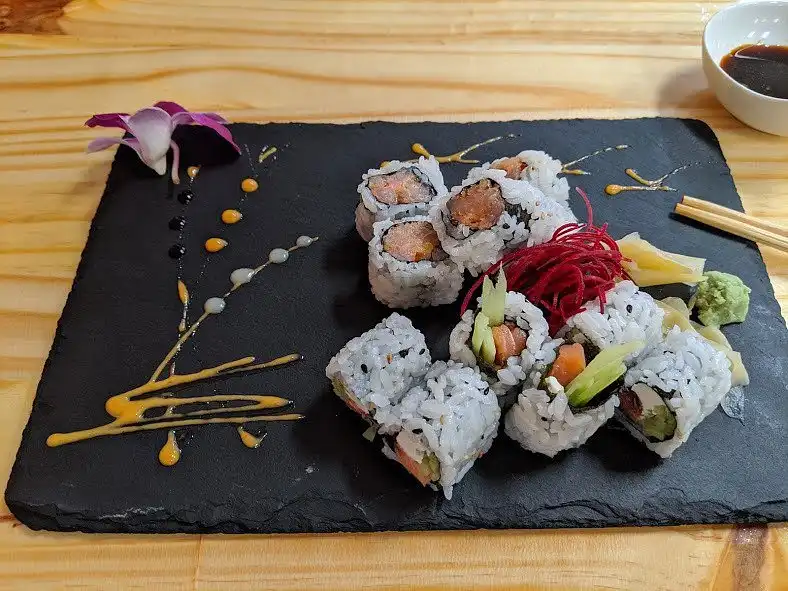 A black slate platter holds an elegant arrangement of sushi rolls, garnished with pickled ginger, wasabi, a purple orchid…