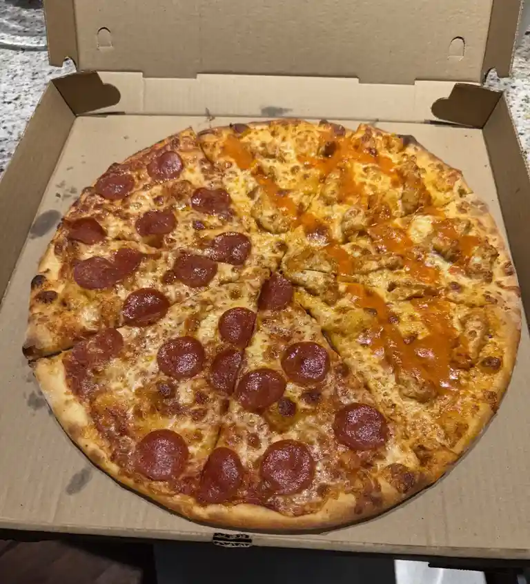A pizza in an open cardboard box is sliced and visibly split down the middle: one half is covered with pepperoni and cheese…