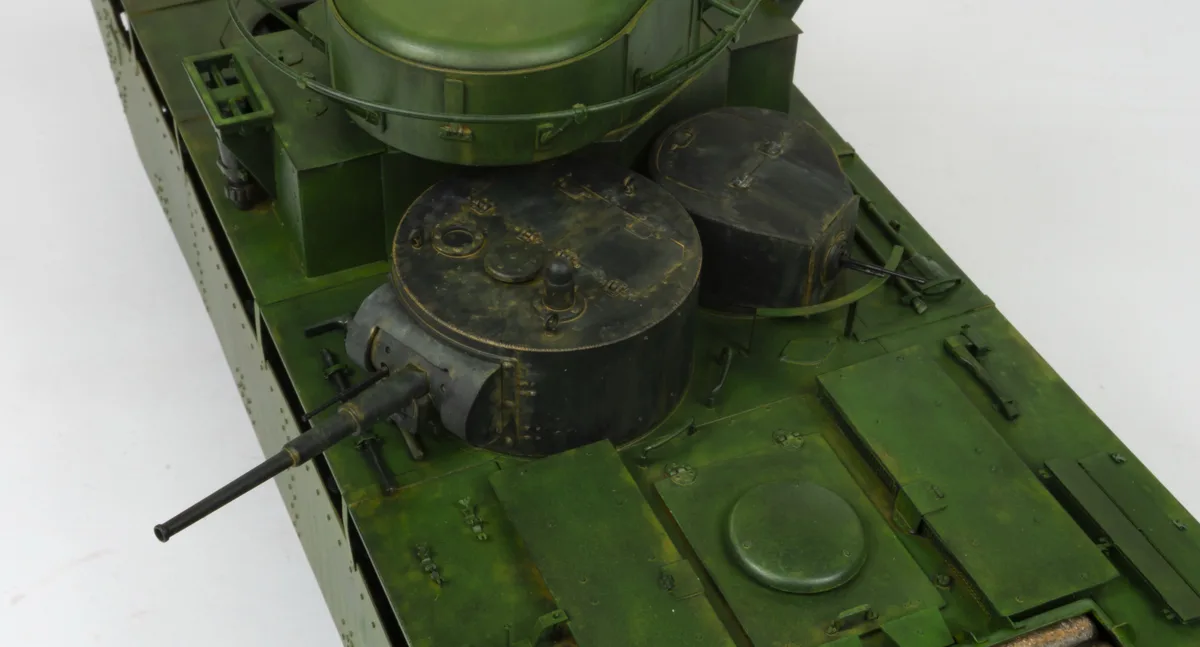 A close-up photo of a detailed green military tank model, showing its turret, gun barrel, and various hatches and panels on…