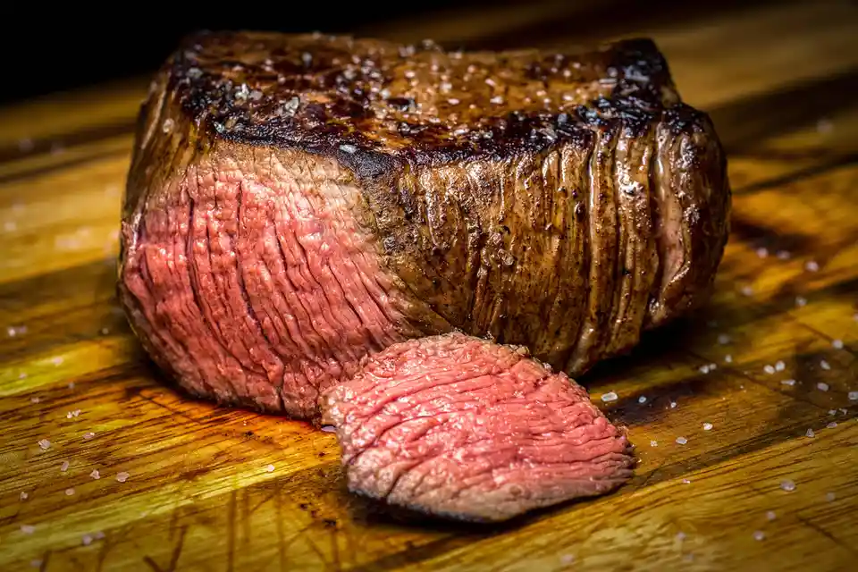A close-up photograph shows a large, juicy steak with a seared, browned crust and a pink, medium-rare interior, resting on a…