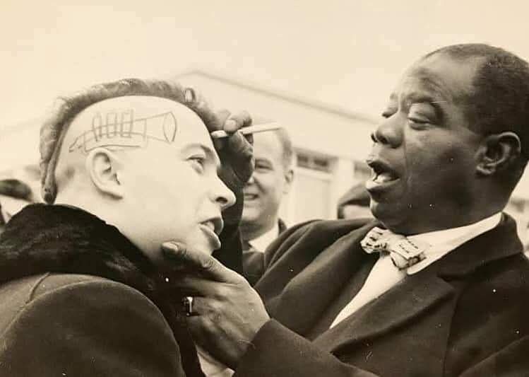 A black-and-white photo shows a Black man in a suit and bowtie drawing a crude diagram of a telescope on the shaved scalp of…