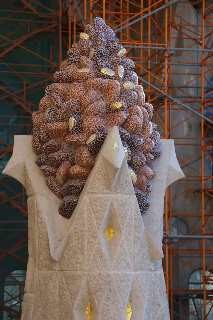 a close-up photograph of a large, ornate sculpture resembling a pinecone, constructed from mosaic tiles in shades of brown…
