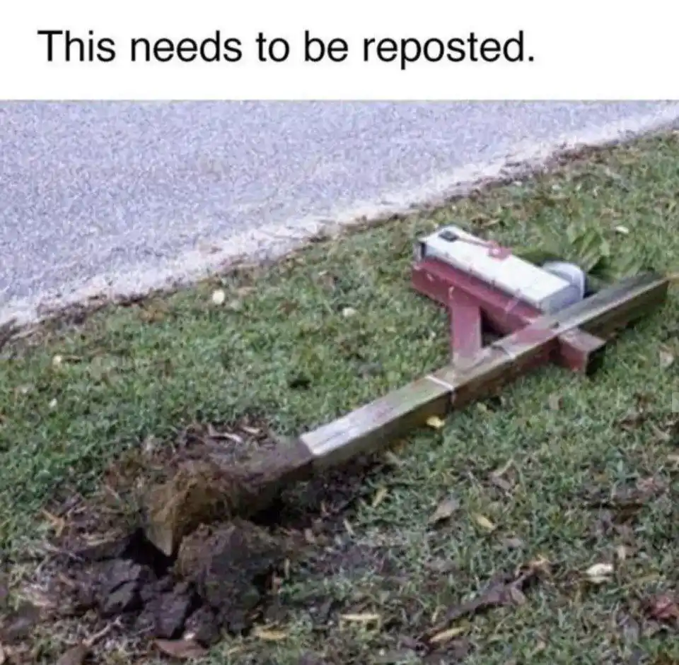 A red and silver mousetrap is set on a grassy area next to a paved surface, with its lever arm extended and a small pile of…