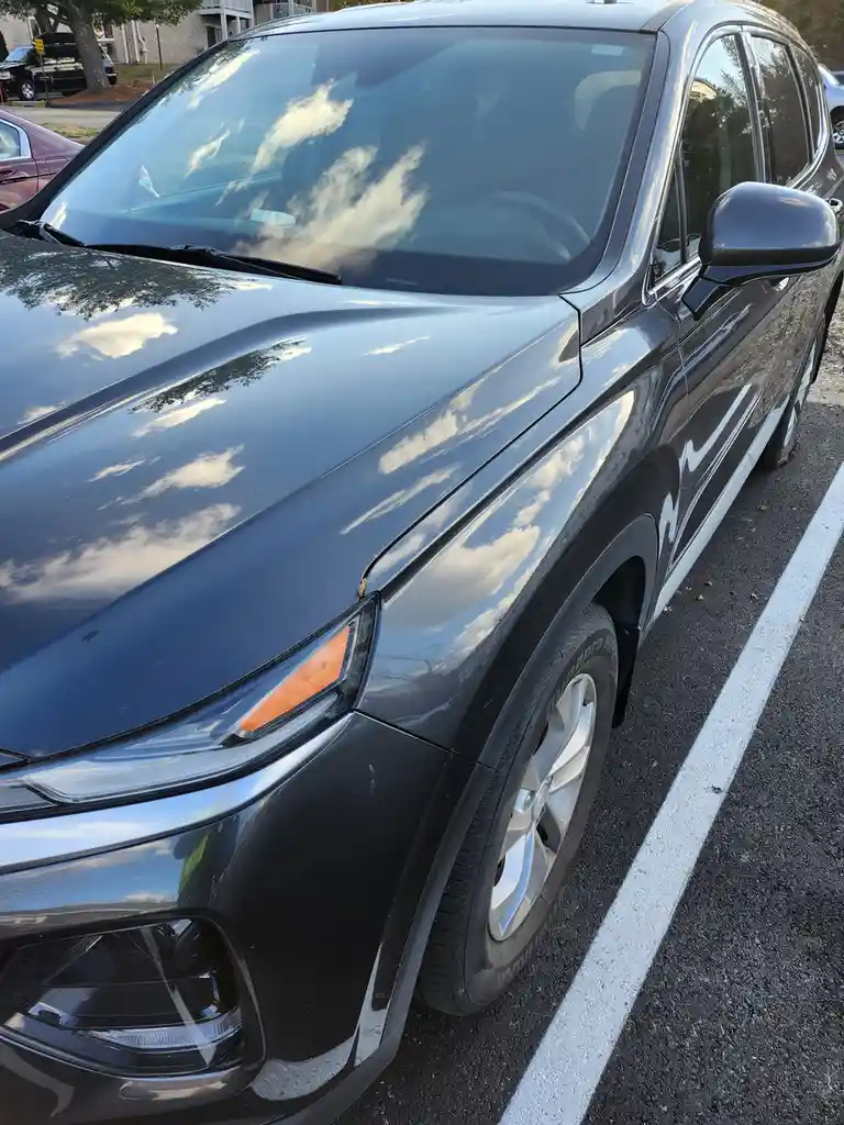 A close-up photo of a shiny black SUV parked in a lot, with clouds and sky clearly reflected on its polished hood and…