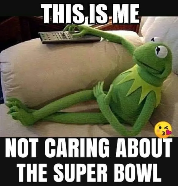 A green Kermit the Frog plush toy is lounging on a beige couch, one arm extended holding a TV remote, with a smug…