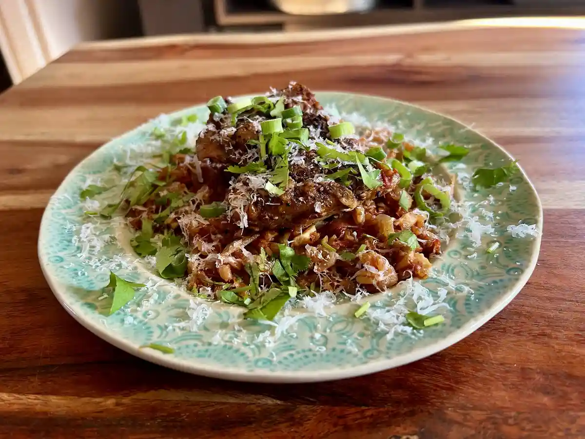 A close-up photo shows a plate of food, likely a pasta or rice dish with meat, garnished with chopped green onions and fresh…