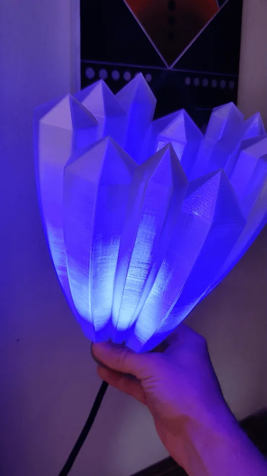 A hand holds a 3D-printed, tulip-shaped lamp with multiple pointed petals, shown in six panels displaying different lighting…
