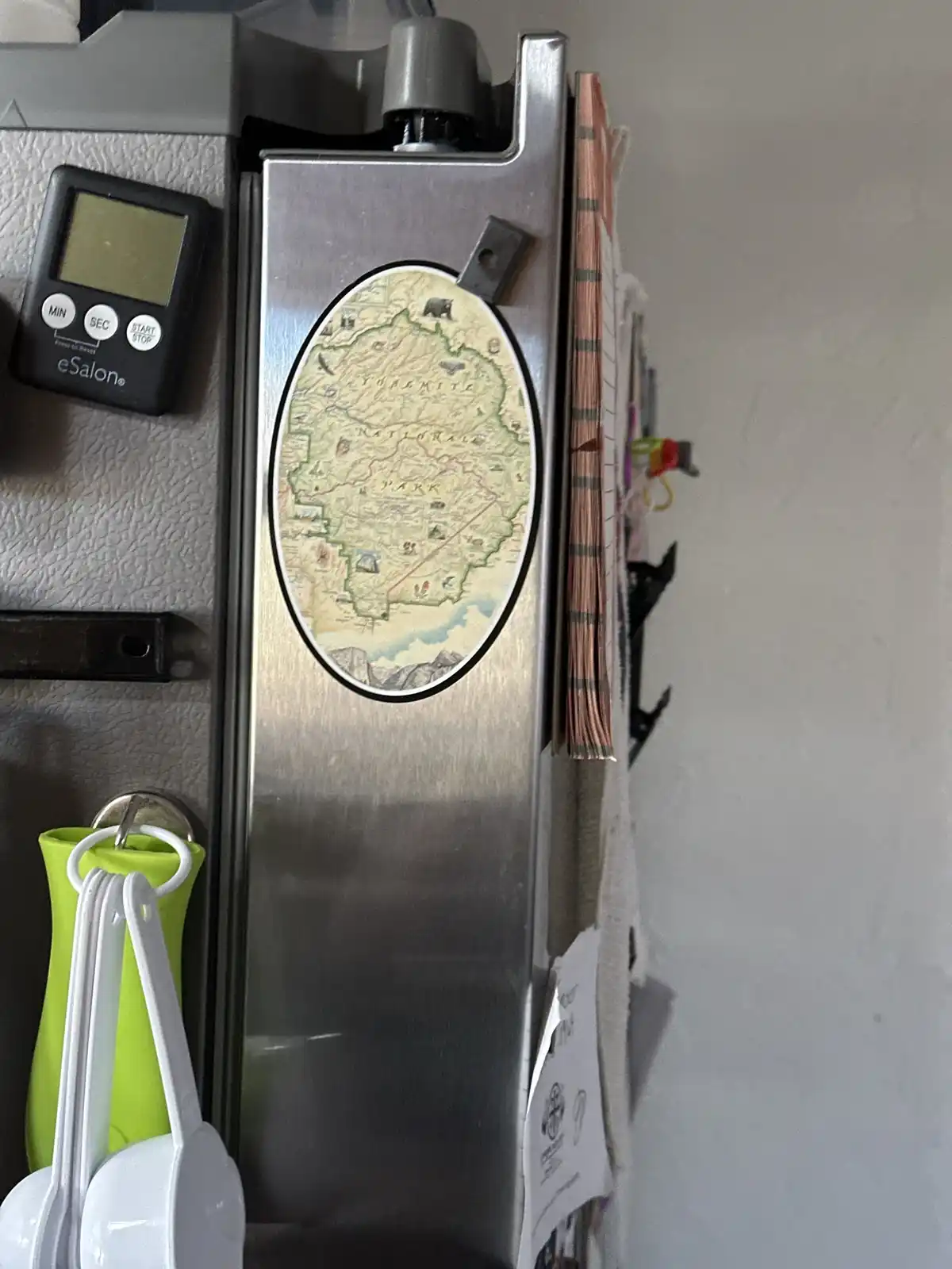 A close-up of a stainless steel refrigerator door with various magnets and kitchen items attached. Prominently featured is…