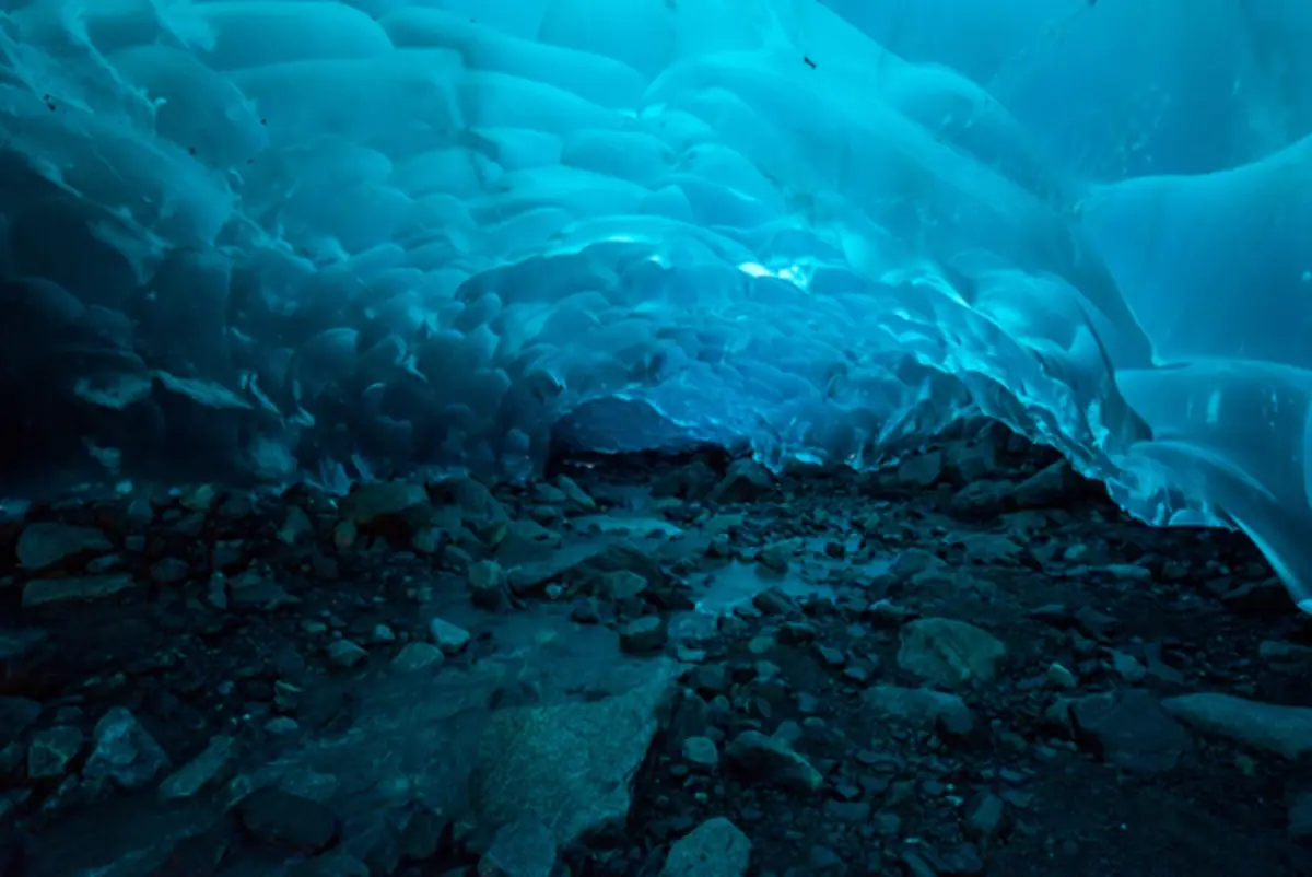 A photo of a blue-lit ice cave with rocky ground, overlaid with the text 'i'm not a fan of the cold'. The image shows the…