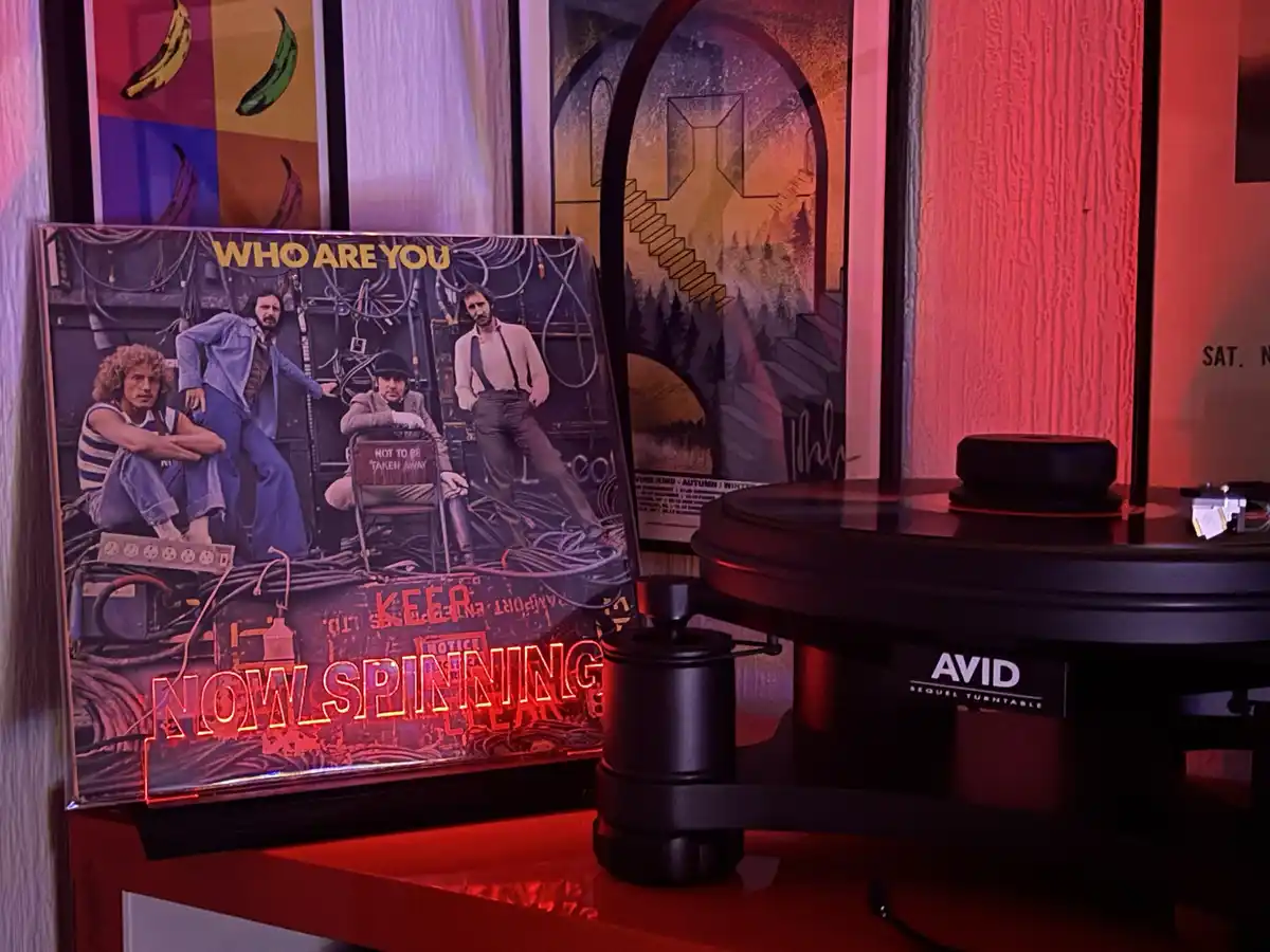 A vinyl record album cover for The Who's 'Who Are You' is propped up next to an AVID Sequel turntable, with glowing red neon…